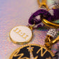 Detailed close-up of the white enamel charm with "11:11" in gold lettering, hanging beside the black compass charm and purple fabric tie