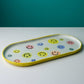 Elongated ceramic serving platter featuring colorful hand-painted smiley faces with bright yellow rim