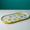 Elongated ceramic serving platter featuring colorful hand-painted smiley faces with bright yellow rim