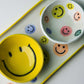 Close-up of ceramic bowl and long platter set decorated with multicolor smiley face illustrations