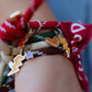 Wrist shot of a person wearing a stack of the colorful Cool Kids cord bracelets with charms and fabric ties, paired with a blue denim jacket sleeve