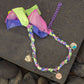 Braided bandana bracelet with multicolour fabric ties and dangling charms displayed on stone surface