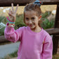 Smiling girl wearing bubble gum pink fleece jogger set displaying peace sign outdoors