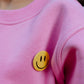Close-up of yellow smiley badge detail on bubble gum pink kids fleece sweatshirt