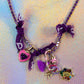 Close-up of the charm cluster on the purple chain, showcasing the pink heart lock, pink/purple carabiner, and the multi-colored gemstone Virgin Mary medal