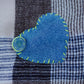 Close-up of stitched denim heart patch with smiley button on navy and denim blue checkered scarf