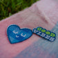 Close-up of heart face and Good Vibes pins on peach and denim blue checkered scarf