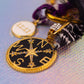 Macro shot focusing on the round black and gold compass charm, accented with cubic zirconia stones, next to the white 11:11 disc