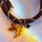 Close-up of the charms on the ebony cord bracelet, clearly showing the peach/brown enamel heart, the bright yellow lightning bolt, and the black enamel star charm