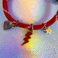 Close-up of the charms on the red cord bracelet, clearly showing the dark grey/black enamel heart, the striking red lightning bolt, and the yellow star charm