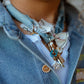 Detail shot of the denim necklace worn around the neck, styled over a white shirt and a light wash denim jacket, emphasizing the fabric texture and charm cluster