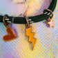 Close-up of the charms on the green cord bracelet, clearly showing the brown/orange enamel heart, the bright yellow lightning bolt, and the small pink star charm