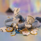 A close-up view of the necklace lying down, showing the texture of the light blue denim fabric and the pile of dangling gold-toned and enamel charms