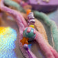 Detail of the Fuzzy Keychain yarns (pink, purple, mint) and the unique drip glaze bead in blue and pink, followed by an orange star bead