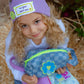 Child holding a blue checkered denim pouch with neon zipper and flower patch