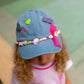 top shot of denim cap worn by child showing game over pin and beads