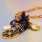 Angled detail shot of the full charm cluster, including the compass, 11:11, and Evil Eye charms, showing a fringed black and purple fabric accent