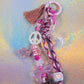 Close-up of glitter graffiti heart key charm featuring tassel, peace sign bead and braided pink cord