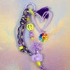 Full view of the chunky beaded keychain with a large lavender heart, purple paracord strap, neon peace sign, and rainbow flower charm