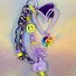 A colorful and chunky Graffiti Heart Key Charm lying showcasing the lilac camera, bow, and purple gummy bear beads