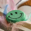 Close-up of green smiley face bath bomb with textured fizz surface and cheerful hand-painted facial design