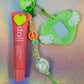 Charm featuring a winged heart pendant and a detailed bead string, posed next to a coral lip balm