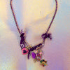 Full view of a dazzling purple rhinestone chain necklace with a chunky charm cluster attached, featuring a pink heart lock, pink carabiner, and colorful jeweled Virgin Mary medal
