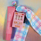 Kawaii Keyring set on a holographic background, featuring the pink slot machine, a pink lip balm, and the light blue/pink/yellow gingham lanyard