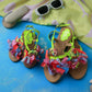 Kids happy sandals with bright green straps and multicolor fabric flowers styled with sunglasses and towel for summer beach look