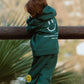 Side view of child wearing galaxy green Kindness is Cool fleece jogger set outdoors with hoodie and matching pants