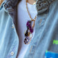 A style shot showing the denim necklace worn with a white t-shirt and light denim jacket, layered beautifully with a separate chunky gold chain necklace and other charms