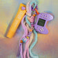 Retro Gamer Key Charm set on a holographic background, showing the purple controller and the yellow lip balm prop, alongside a pastel beaded string