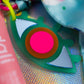 Close-up of the Evil Eye Charm in green acrylic, highlighting the neon pink center and mirrored silver details