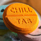 Back view of orange smiley bath bomb showing embossed Chill Tab lettering and round pressed shape