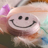 Close-up of pink smiley face bath bomb with textured fizz surface and bold black facial design for fun and relaxing bath time