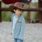 Side view of boy wearing Pocket Full of Dreams kids denim shirt with cowboy hat