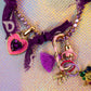Close-up shot emphasizing the pink enamel heart lock charm with a large central purple stone, connected to the purple jeweled chain and fabric tie