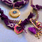Detailed shot focusing on the pink carabiner clasp, purple tassel, gold bow, and the colorful Virgin Mary charm against the iridescent background