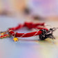 Close-up side view of the red rope bracelet and its charms (yellow star in focus), showing the textured cord and the black/white frayed fabric tie in the background