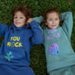 Two kids lying on grass wearing You Rock denim blue mint mellow fleece jogger sets